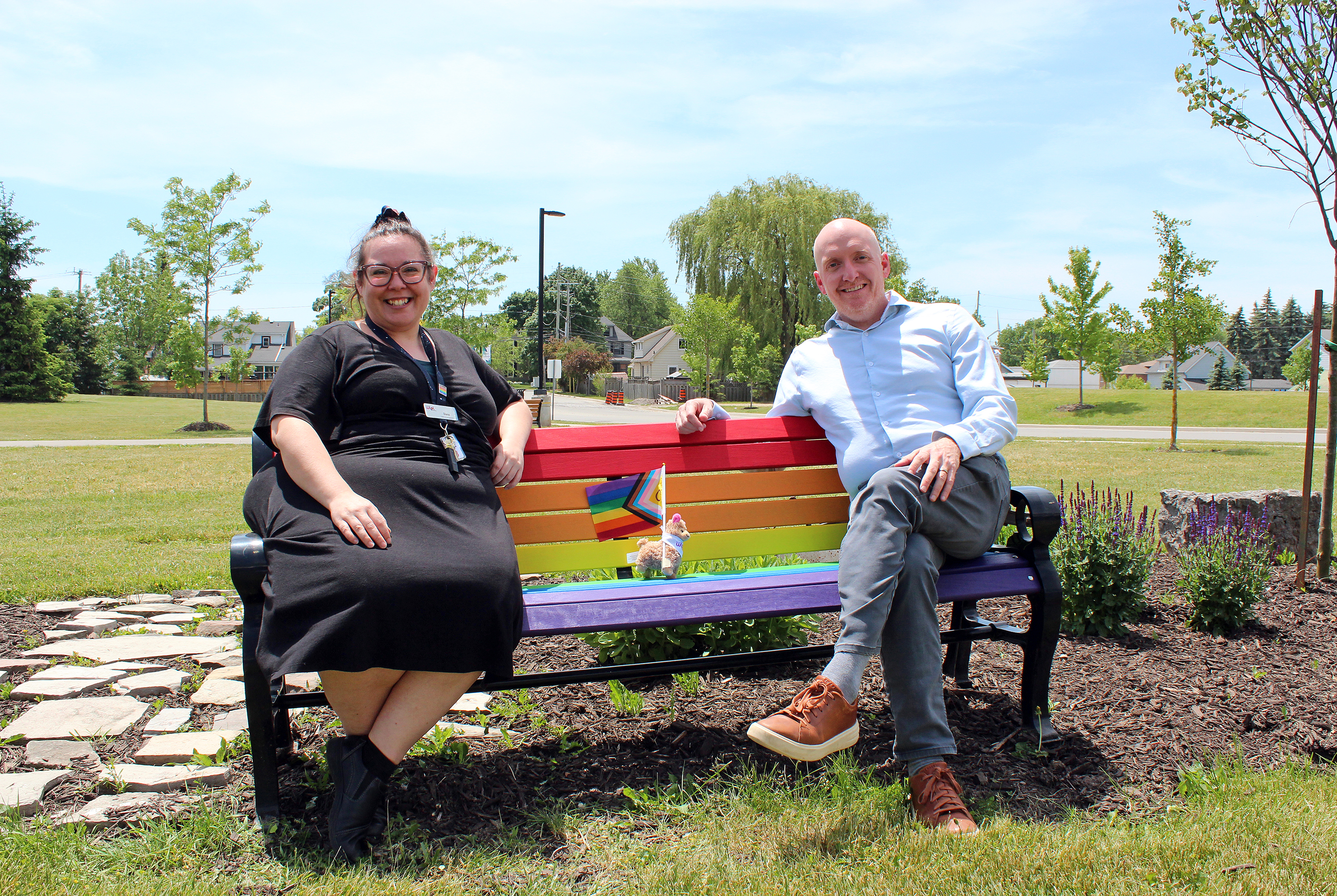 Two people sit on a bench painted with Pride colours