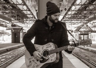 singer M. T. Walker standing on a platform playing an acoustic guitar