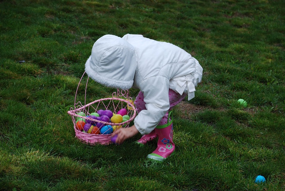 small child collecting colourful eggs in an Easter basket on green grass 