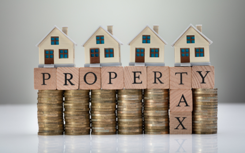 Small wooden houses on stacks of coins with text that says Property Tax