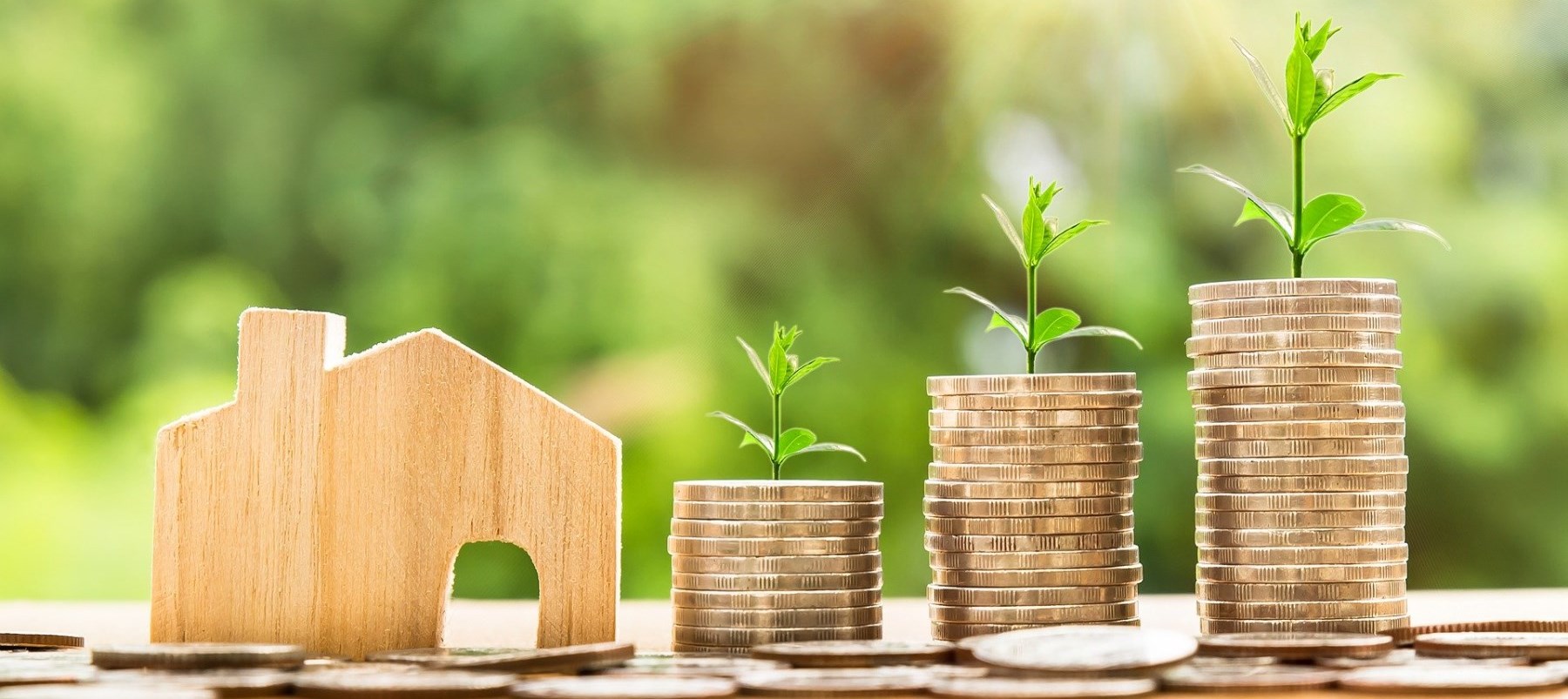 Close up of toy wooden house and growing piles of coins