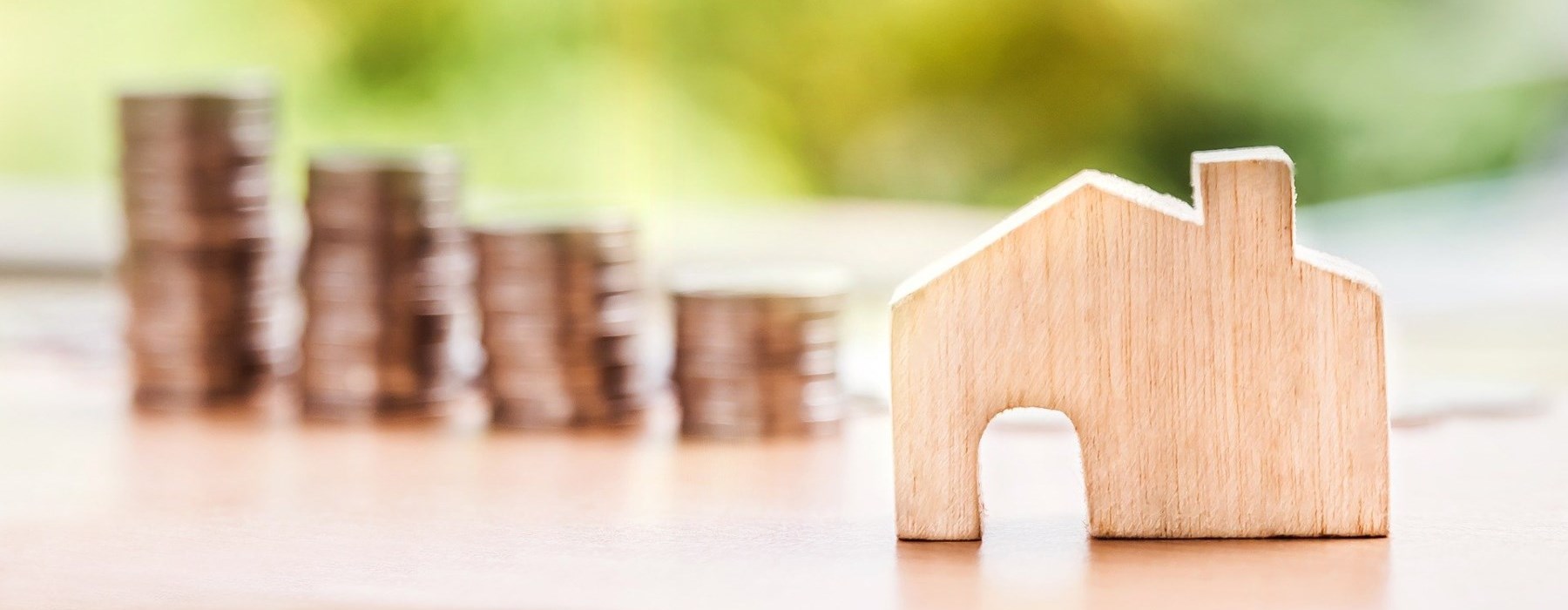 Wooden toy house beside growing pile of coins