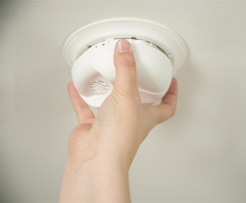 person's hand installing smoke alarm in ceiling