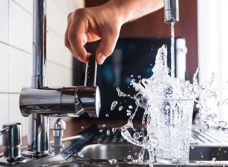 Hand turning on faucet to fill glass with water